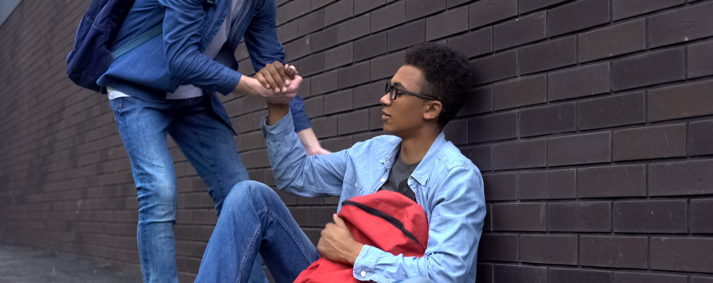 Teenage Student Giving Helping Hand To Bullied Afroamerican Boy Stop