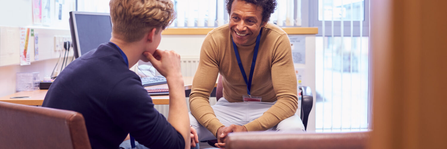 Male College Student Meeting With Campus Counselor Discussing Mental Health Issues