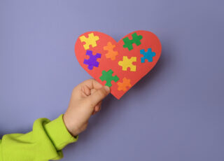 A big red heart with details of colored puzzles inside in a child's hand there is a symbol of autism. World Autism Day