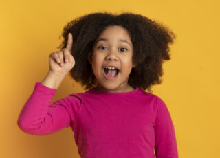 I Have Idea. Little african american girl pointing finger up and looking at camera, standing over yellow studio background with free space